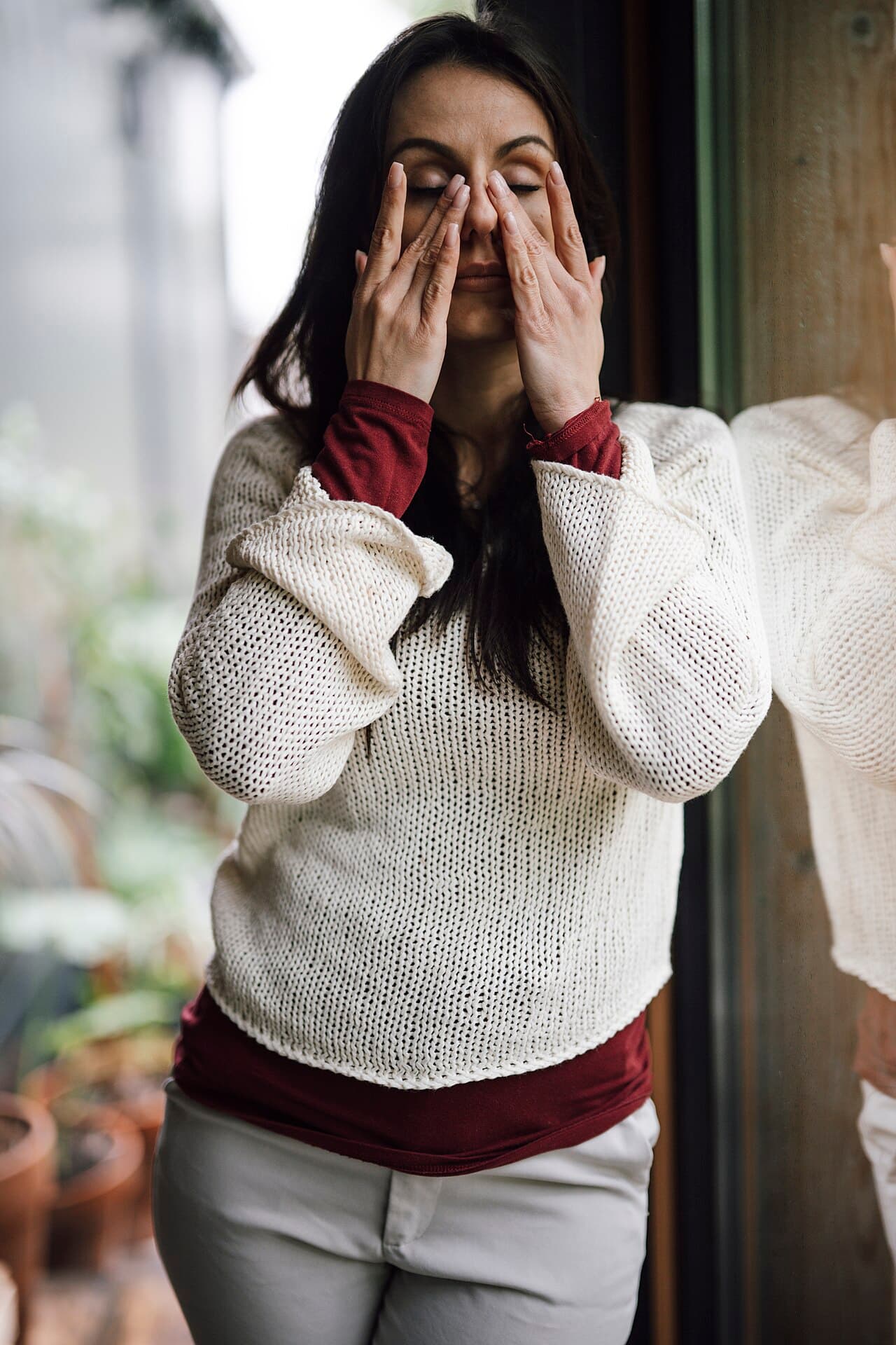 Femme anxieuse, mains sur le visage près d'une fenêtre