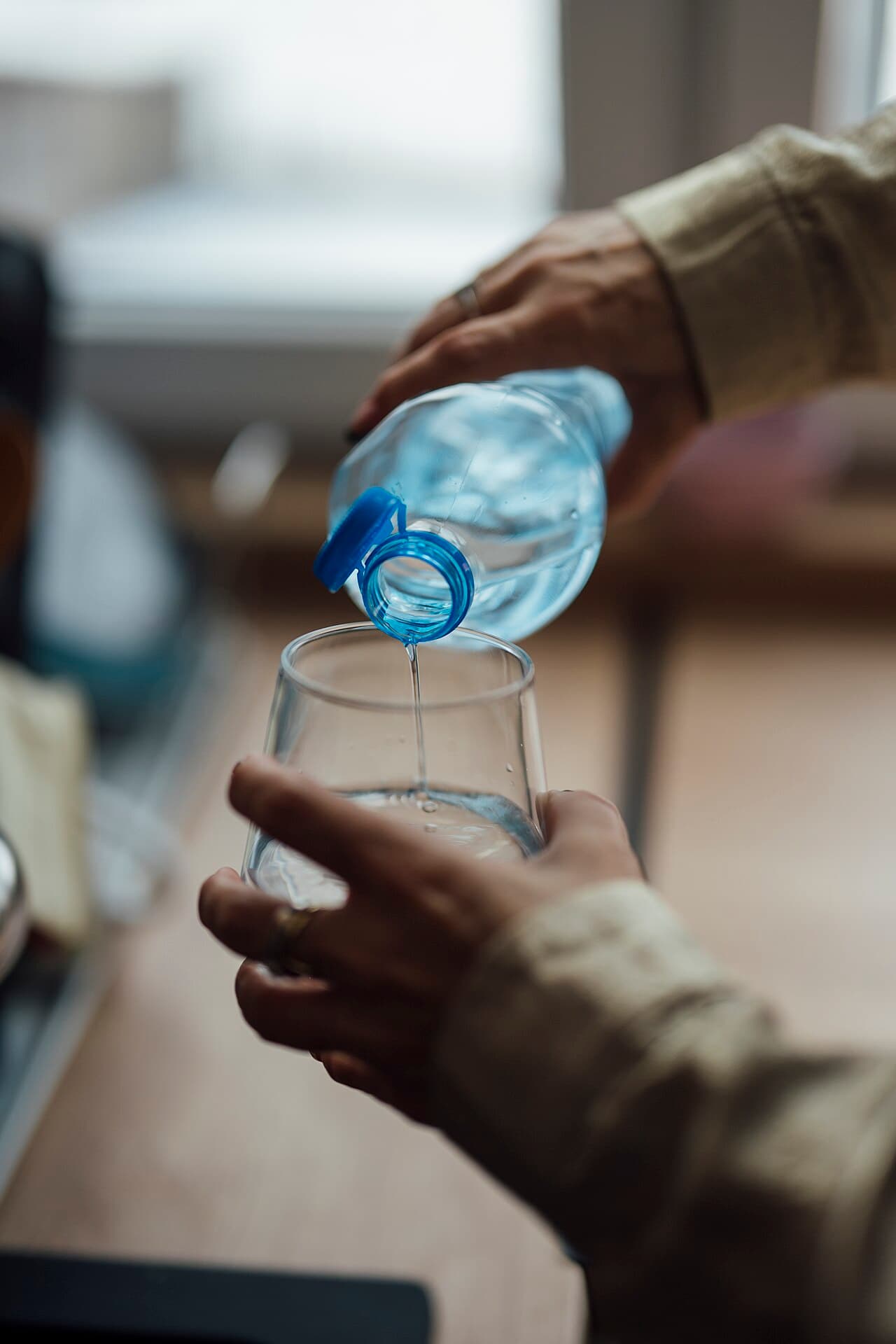 Mains versant de l'eau d'une bouteille dans un verre